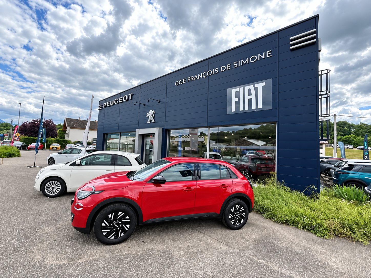 Façade bleue d'un garage Peugeot et Fiat devant laquelle sont garées une voiture rouge et une Fiat blanche.